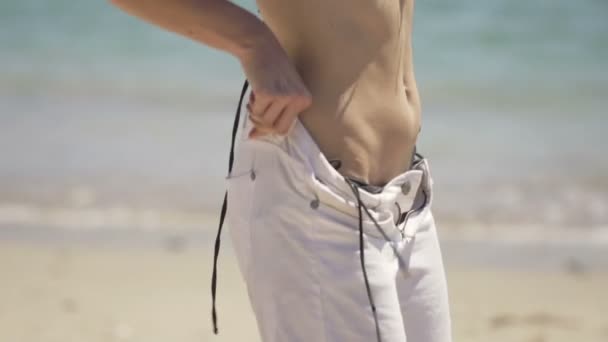 Женщина надевает шорты стоя на пляже — стоковое видео