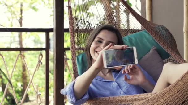 Жінка фотографує селфі з мобільним телефоном на гамаку — стокове відео