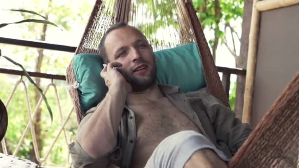 Hombre hablando en el teléfono celular mientras que miente en la hamaca — Vídeo de stock