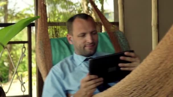 Бизнесмен смотрит кино на планшетном компьютере на гамаке — стоковое видео