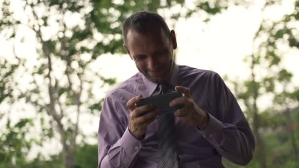 Homem de negócios jogando jogo no smartphone no parque — Vídeo de Stock