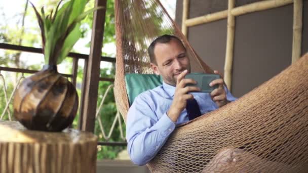 Hombre de negocios jugando juego en el teléfono inteligente en hamaca — Vídeo de stock