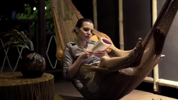 Женщина читает книгу лежа на гамаке — стоковое видео