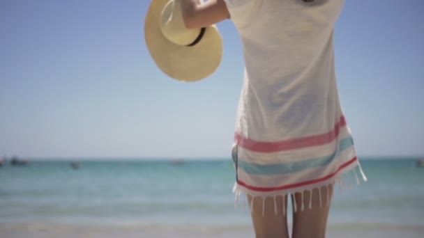 Mujer poniéndose el sombrero de pie en la playa — Vídeos de Stock