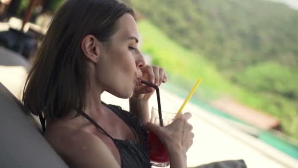 Женщина расслабляется и пьет коктейль на лежаке — стоковое видео