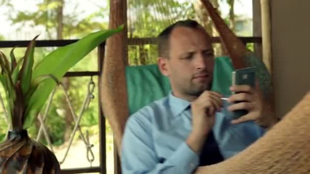 Бизнесмен рассчитывает данные по смартфону на гамаке — стоковое видео