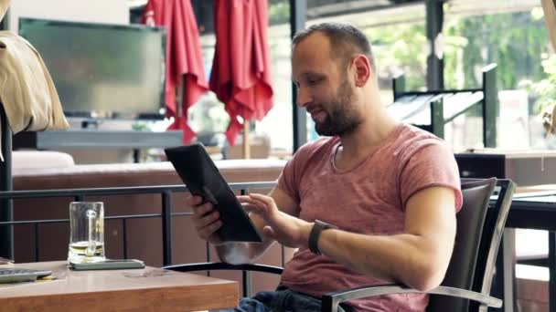 Человек за планшетным компьютером и пить пиво в кафе — стоковое видео