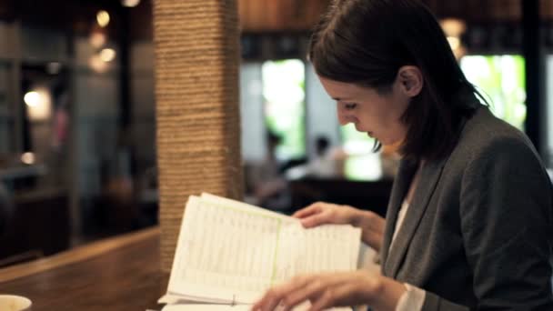 Бизнесвумен читает документы, сидящие в кафе — стоковое видео