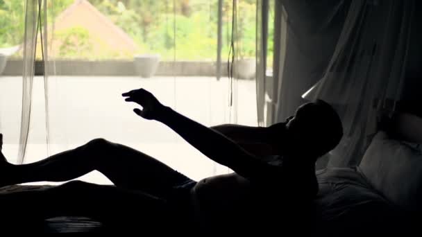 Mann wacht auf und streckt Arme auf dem Bett aus — Stockvideo