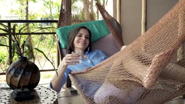 Женщина пьет и поднимает тосты на гамаке — стоковое видео