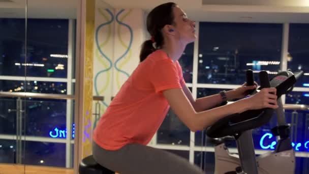 Woman listen to music and riding stationary bike — Stock Video