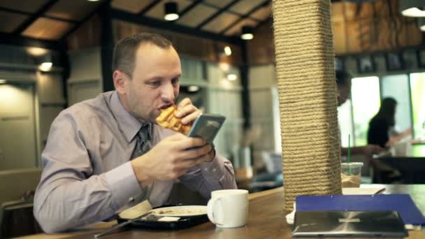 Hombre de negocios con teléfono inteligente beber y comer en la cafetería — Vídeo de stock