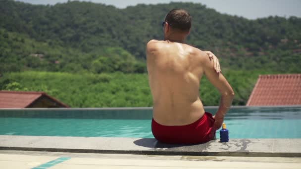 Mann trägt Sonnencreme am Pool auf — Stockvideo
