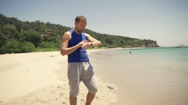 Бегун проверяет время и пульс на умных часах на пляже — стоковое видео