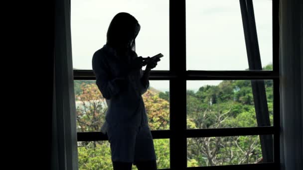 Woman using smartphone standing by window — Stock Video