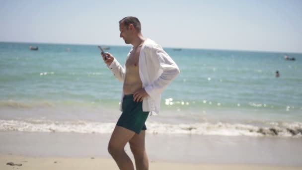 Man using smartphone and walking on beach — Stock Video