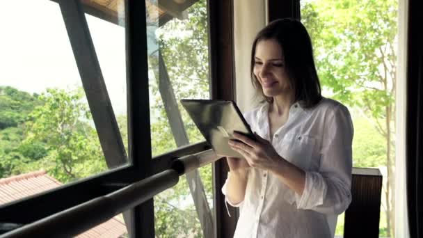 Mujer usando tableta ordenador de pie por ventana — Vídeo de stock