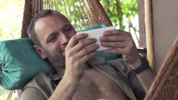 Man playing game on smartphone on hammock — Stock Video