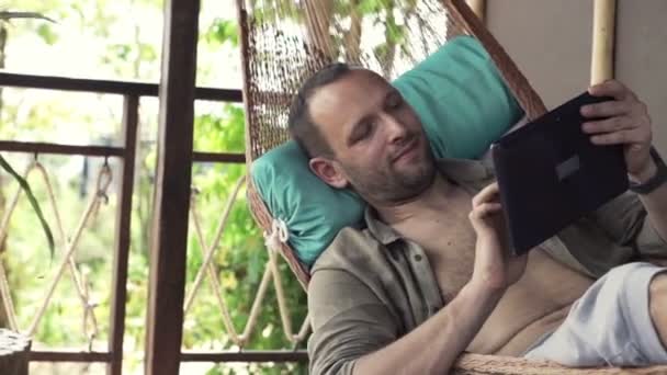 Hombre usando la computadora de la tableta en la hamaca — Vídeos de Stock