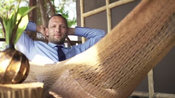 Glücklicher Geschäftsmann entspannt sich auf der Hängematte auf der Terrasse — Stockvideo