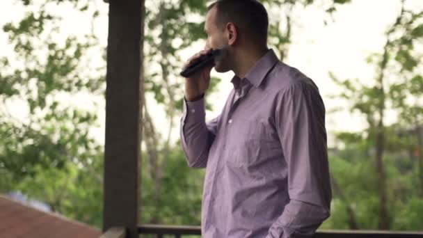 Бизнесмен бреет бороду с электробритвой на террасе — стоковое видео