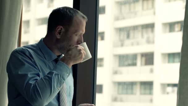 Бизнесмен пьет кофе и смотрит в окно — стоковое видео