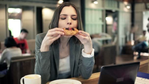 Businesswoman eating tasty croissant for lunch in cafe — Stock Video