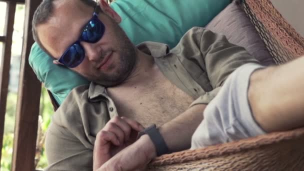 Man met smartwatch liggend op de hangmat — Stockvideo