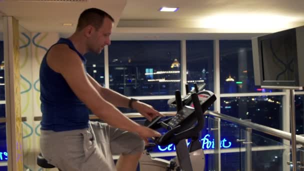 Man med smartwatch ridande stationär cykeln i gym — Stockvideo