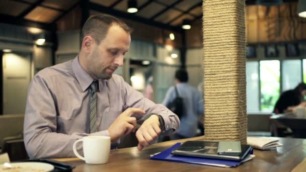 Joven hombre de negocios con reloj inteligente sentado en la cafetería — Vídeos de Stock