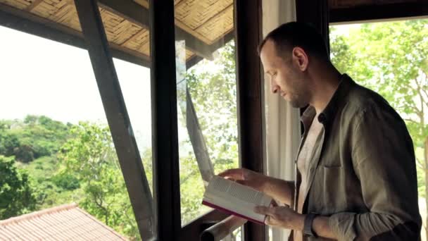 Uomo lettura libro in piedi vicino alla finestra — Video Stock