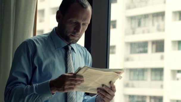 Бізнесмен читає газету, стоячи біля вікна — стокове відео