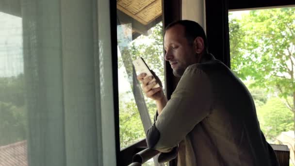 Hombre usando el teléfono inteligente de pie por ventana — Vídeo de stock