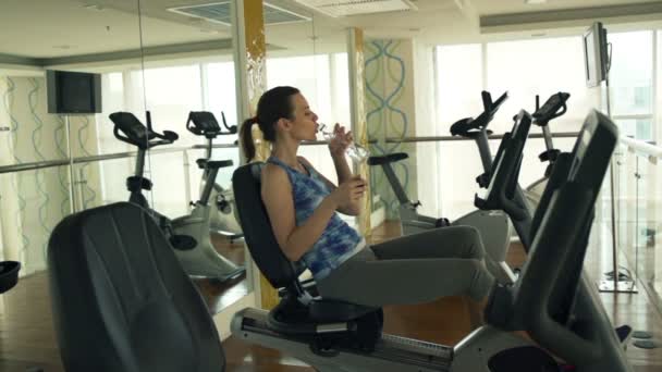 Γυναίκα πόσιμο νερό στο στατικό ποδήλατο στο γυμναστήριο — Αρχείο Βίντεο