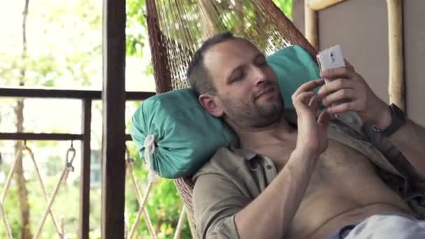 Young man with smartphone lying on hammock — Stock Video