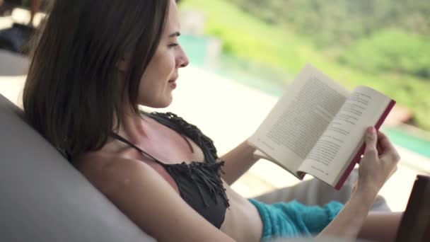 Kvinna på solarium läser bok av poolen — Stockvideo