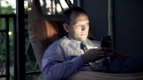 Бизнесмен использует смартфон на гамаке — стоковое видео