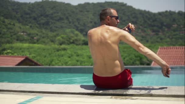 Человек наносит солнцезащитный крем у бассейна — стоковое видео