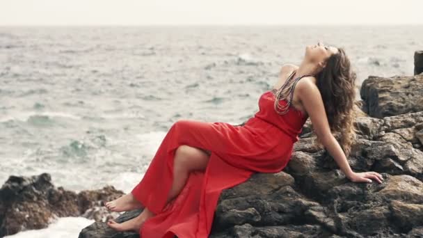 Mujer coqueteando con la cámara sentado en las rocas junto al mar — Vídeos de Stock