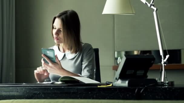 Affärskvinna med smartphone sitter vid skrivbordet på kontoret — Stockvideo