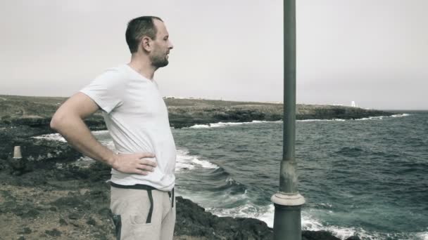 Manliga jogger vilar stående på klipporna vid havet — Stockvideo