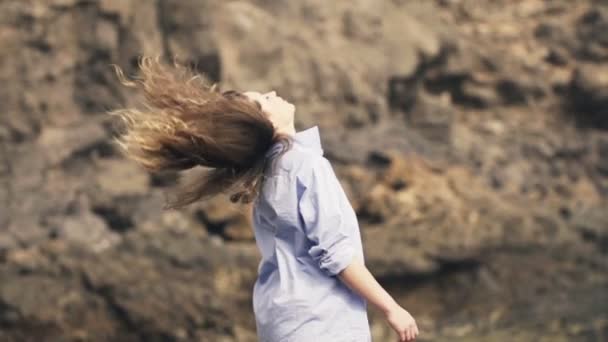 Женщина бросает волосы, стоя на камнях — стоковое видео