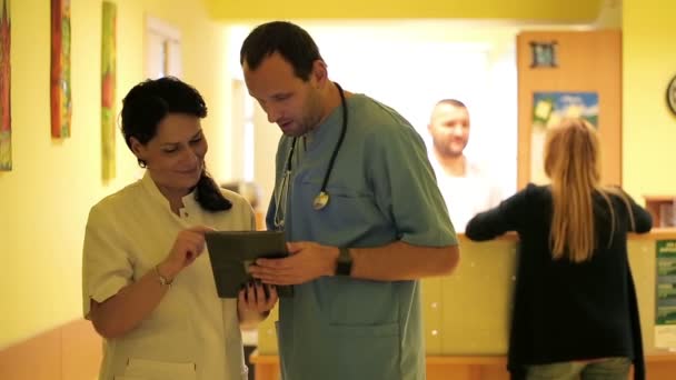 年轻医生在医院大厅里谈论平板电脑 — 图库视频影像