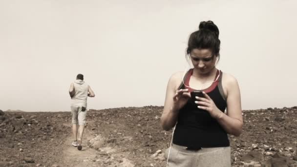 Γυναίκα που χρησιμοποιούν smartphone και άνθρωπος τζόκινγκ στην έρημο — Αρχείο Βίντεο