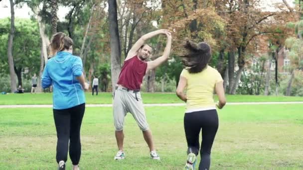 Uomo che si allunga nel parco, donne che fanno jogging che corrono — Video Stock