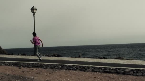 Mujer corriendo a través del paseo marítimo por el mar — Vídeos de Stock