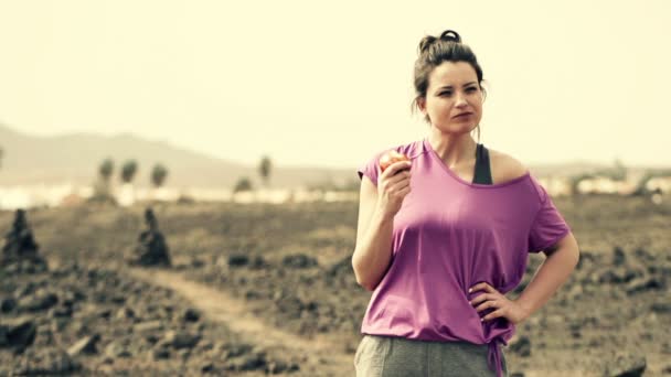 Жінка їсть яблуко, що стоїть на пустелі — стокове відео