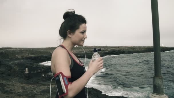 Mujer bebiendo agua mientras está de pie sobre rocas por mar — Vídeo de stock