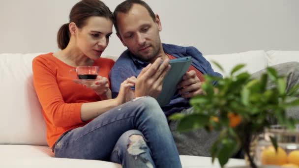 Pareja con tablet ordenador sentado en el sofá en casa — Vídeos de Stock
