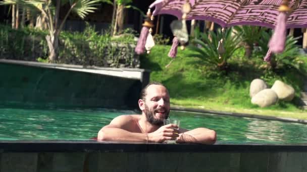 Счастливый мужчина пьет коктейль в бассейне — стоковое видео